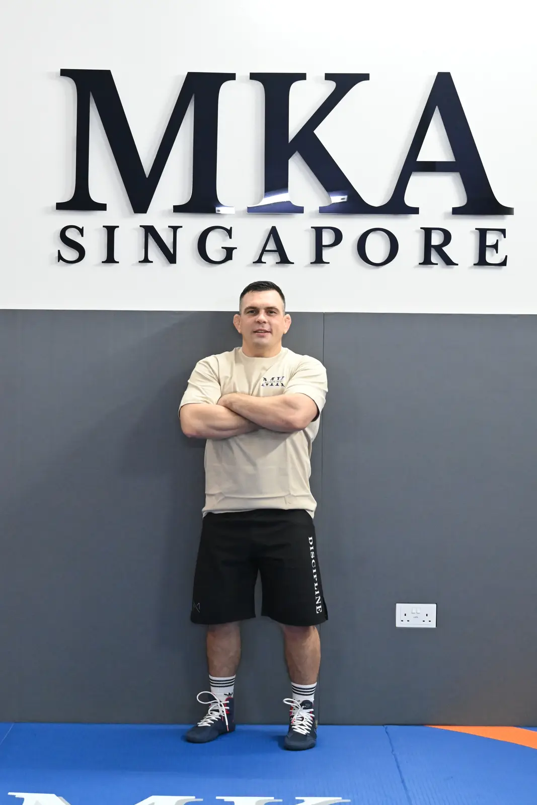 Head coach Artem Kotov standing on the blue academy mat